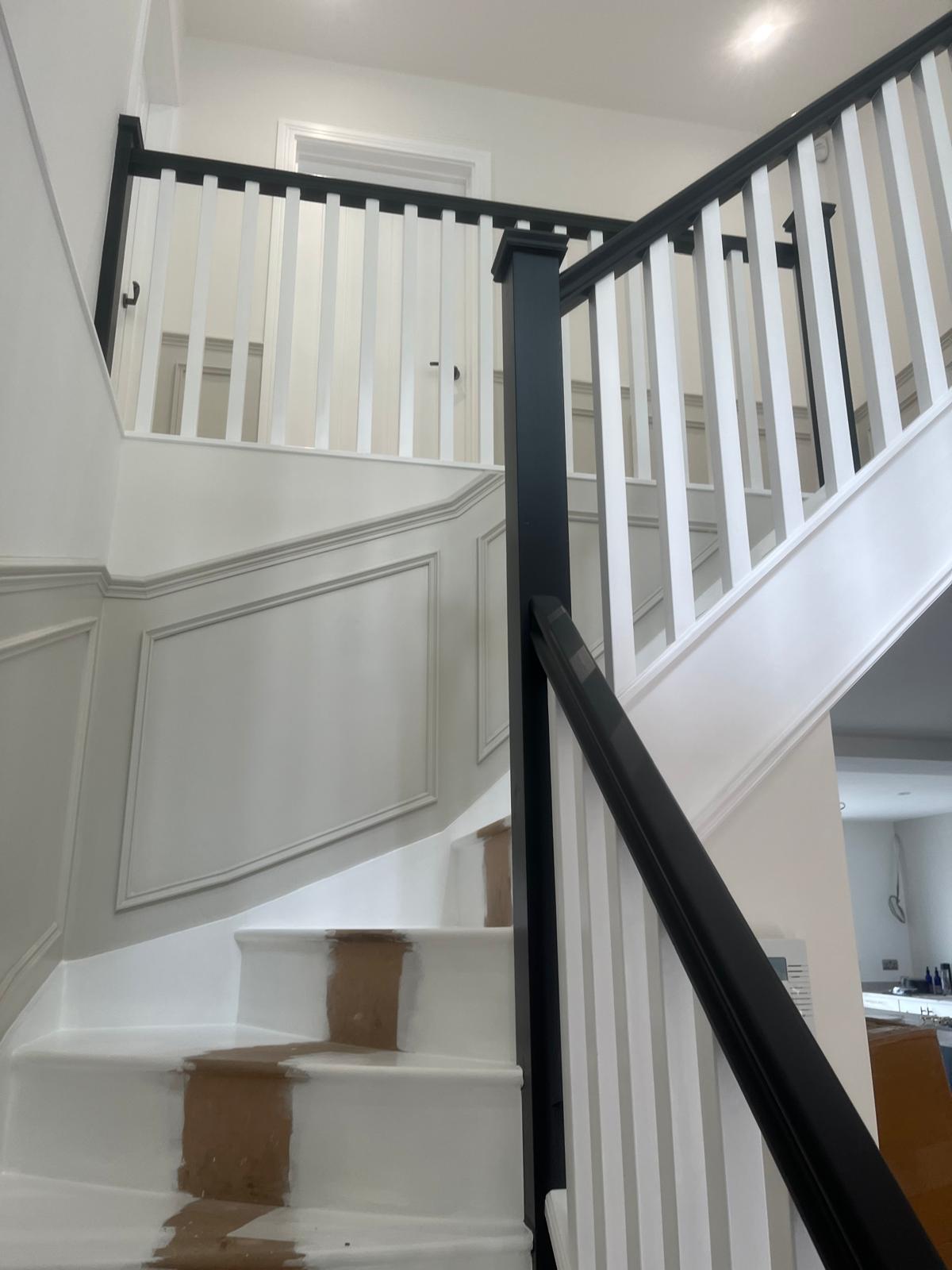 Two-tone staircase with black handrail & panelled walls